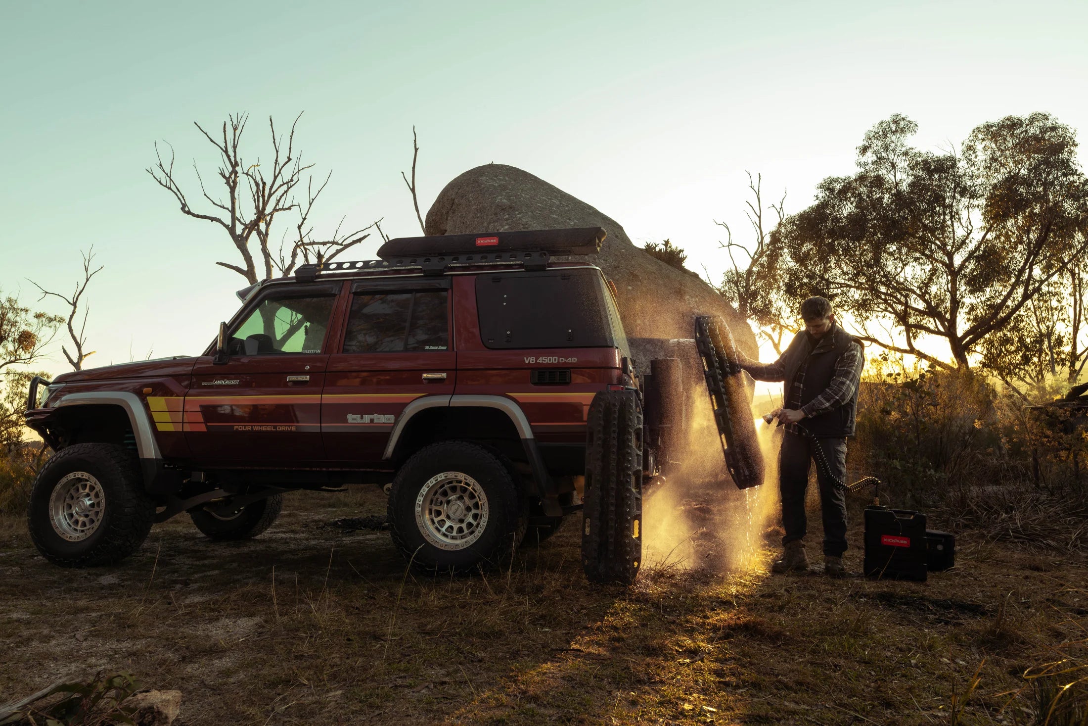 A camper rinses recovery gear beside a four-wheel drive at sunset in the Australian bush