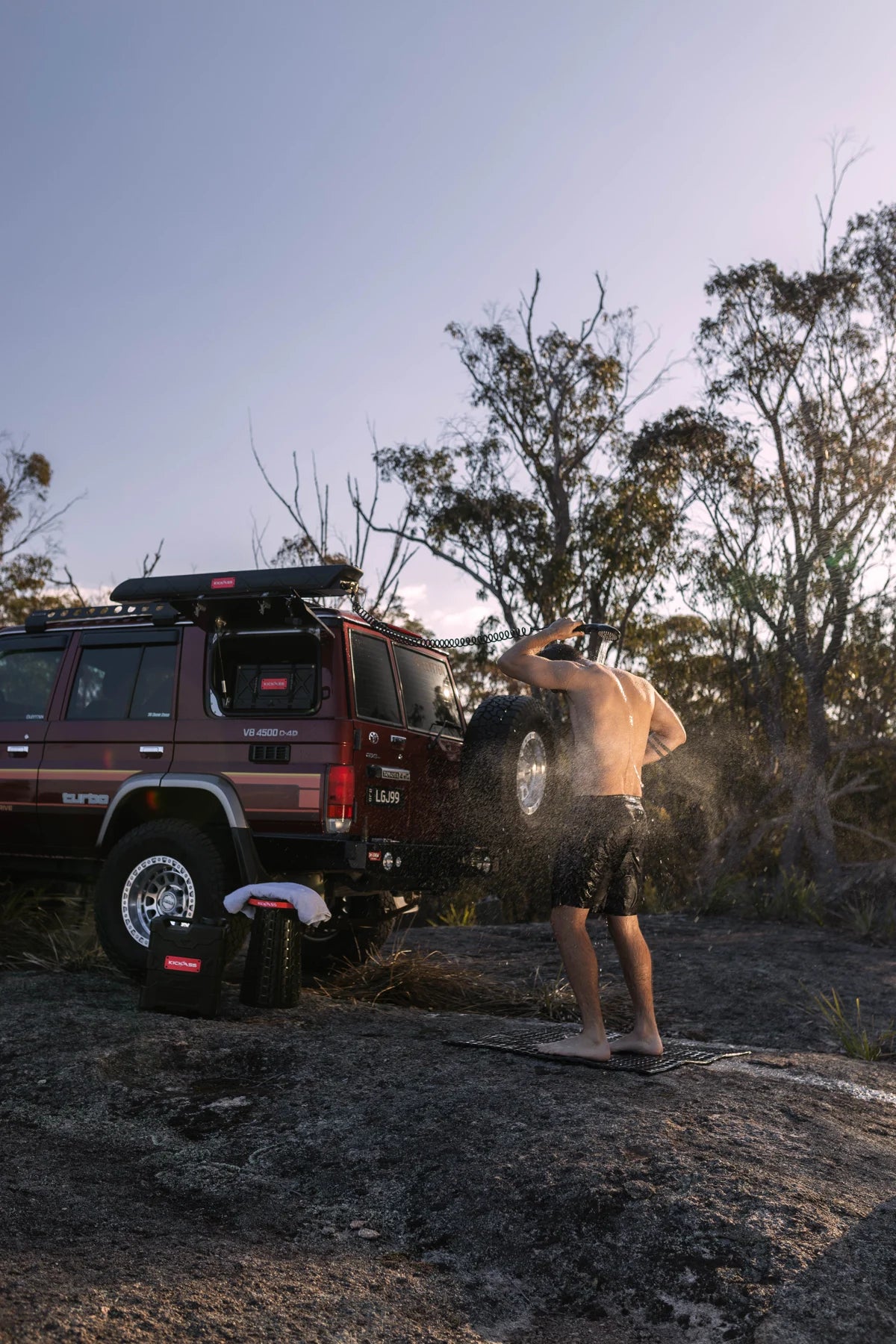 Camper showering beside a four-wheel drive with AquaBoss water systems at camp